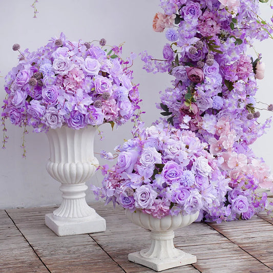 Two white urns filled with purple and pink flowers on a wooden floor.