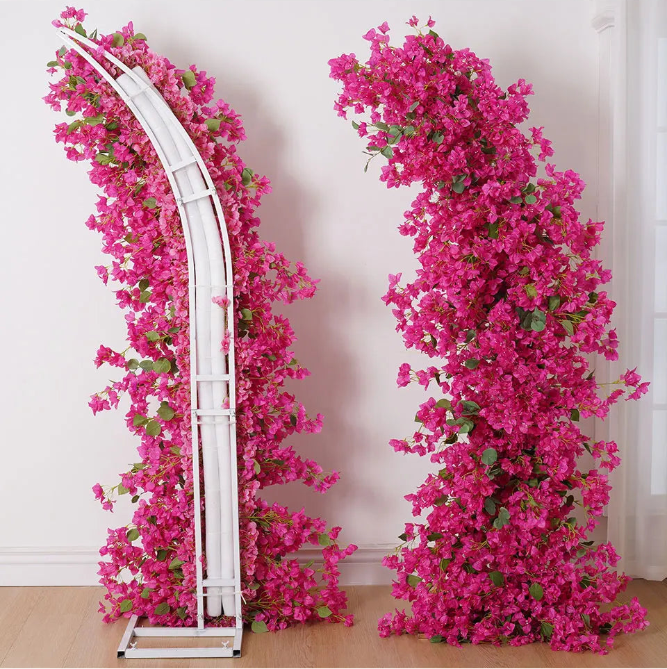 Decorative arch and tall floral stand with pink flowers against a white wall.