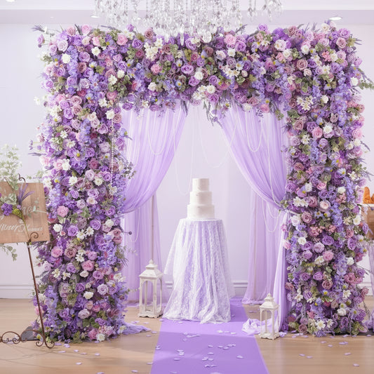 Decorative floral arch with purple and white flowers, draped with fabric, and a cake underneath, branded 'weddingstoryshop Flower'.