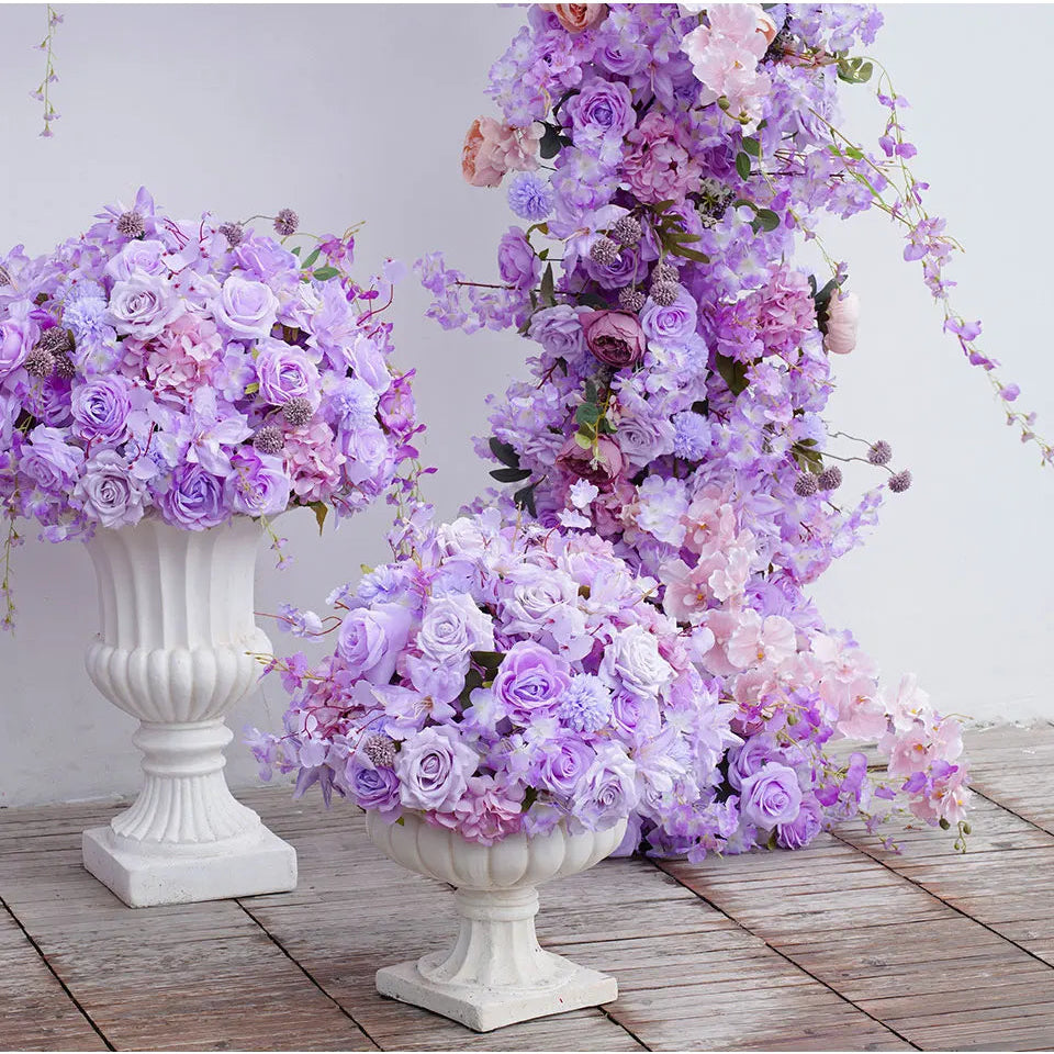 Decorative floral arrangements in white urns on a wooden floor with a light gray background
