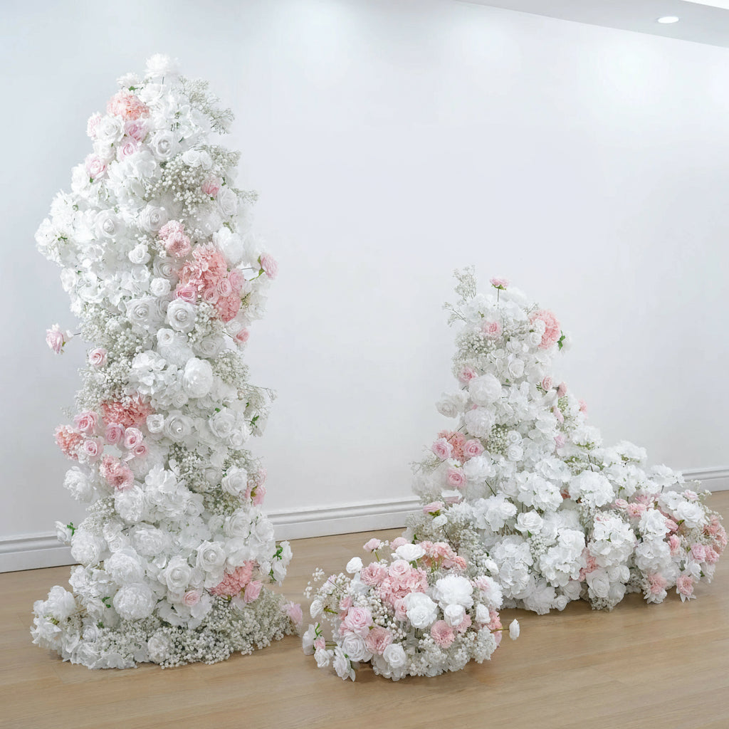 Decorative floral arrangements with white and pink flowers on a wooden floor against a white wall.