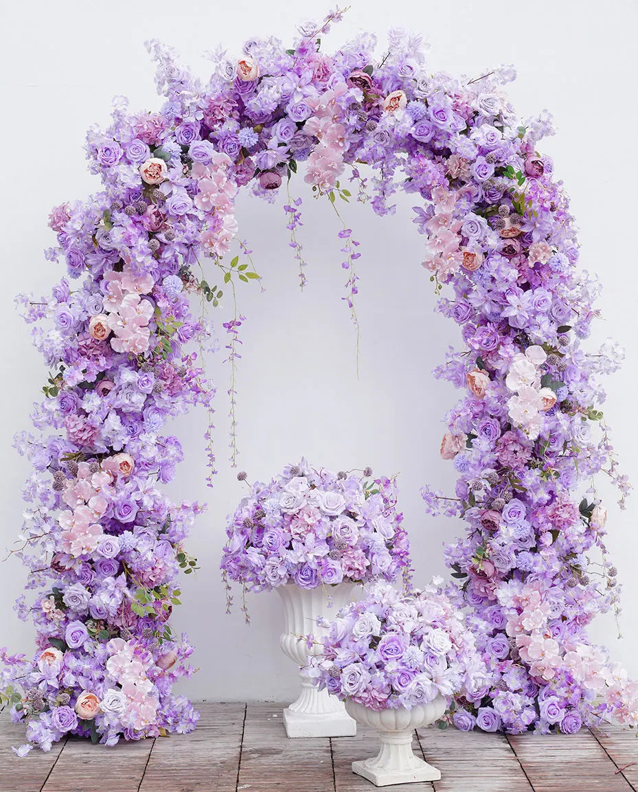 Floral arch and vases with purple and white flowers on a wooden floor.