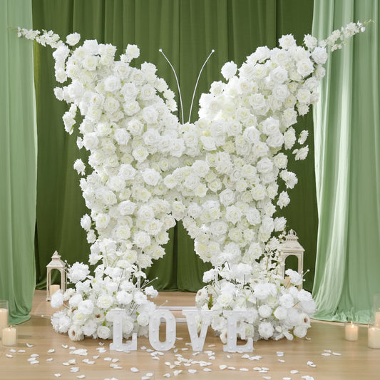 Floral arrangement shaped like a butterfly with 'LOVE' letters on a wooden floor against green curtains.