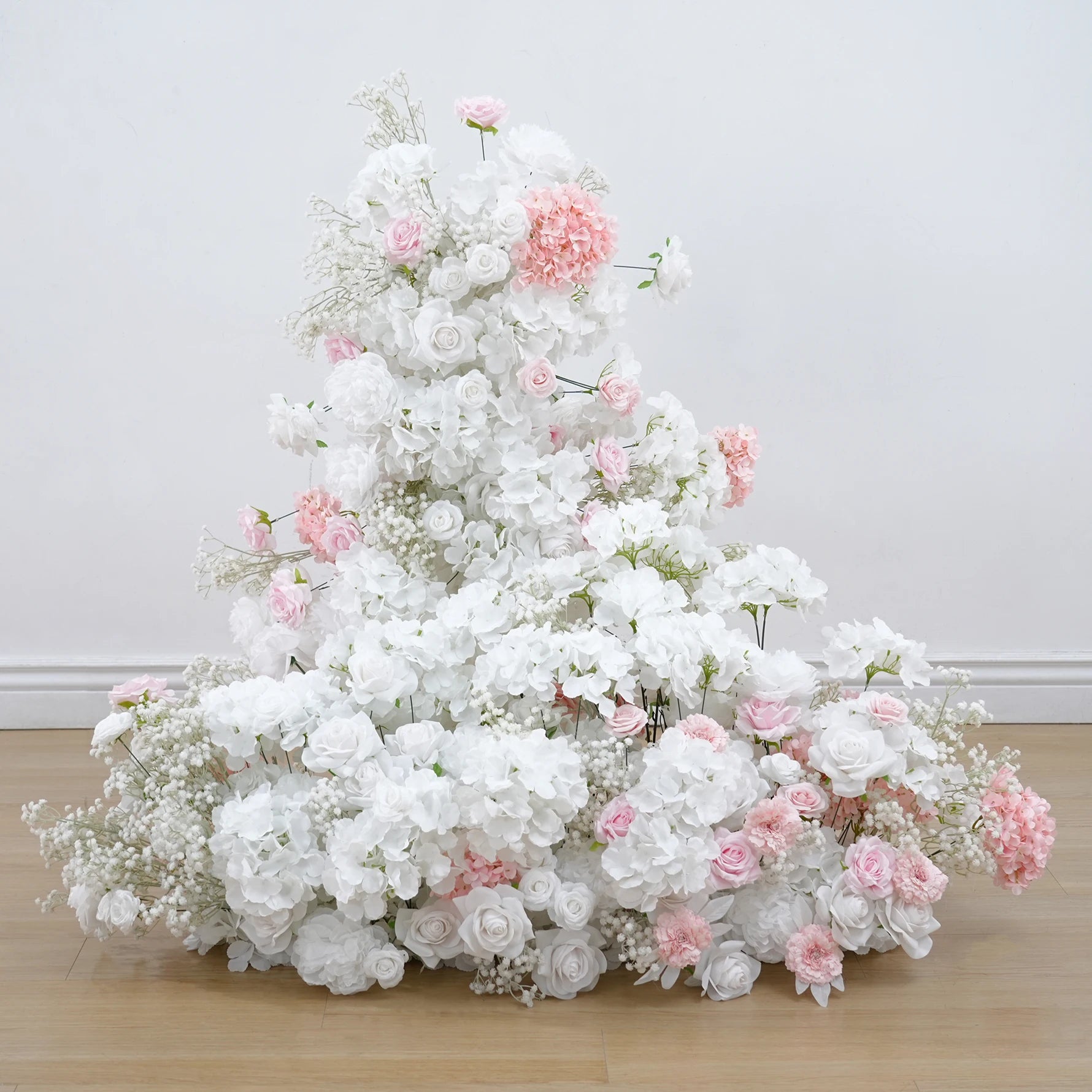 Floral arrangement with white and pink flowers on a wooden floor against a light gray wall.