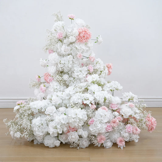 Floral arrangement with white and pink flowers on a wooden floor against a light gray wall.