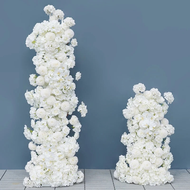 Two tall arrangements of white flowers on a wooden floor with a blue background